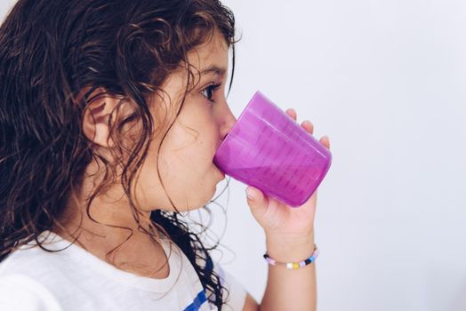 portrait of a little girl rinsing her mouth after brushing teeth in the bathroom before going to bed after taking a shower, kids hygiene concept, copy space for text