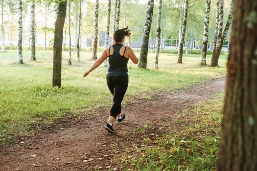 A charming brunette woman plus-size body positive practices sports in nature.