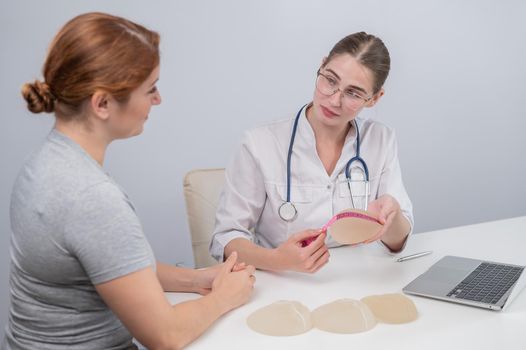 A plastic surgeon measures breast implants with a centimeter tape and demonstrates to a female patient