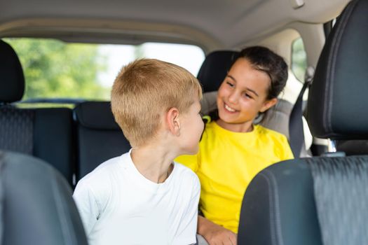 Happy kids, adorable toddler girl with teenager brother sitting together in modern car locked with safety belts enjoying family vacation trip on summer weekend.