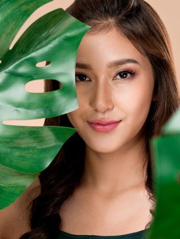 Closeup portrait of young ardent woman with healthy fair skin holding big green leaf near her face. Skin care beauty care concept.