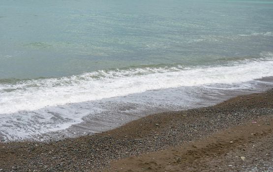 Sea shore with pebbles, wet sea pebbles on the beach and quiet sea surf. Restless sea and waves