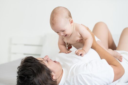 Mother and child on a white bed. Mom and baby boy in diaper playing in bedroom. Parent and little kid relaxing at home. Family having fun together