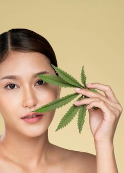Closeup portrait of young ardent girl with healthy fresh skin holding green hemp leaf. Combination of beauty and cannabis concept.