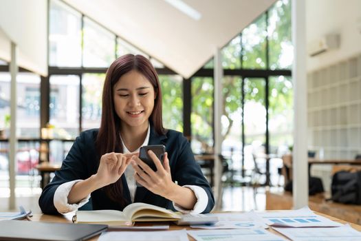 Smiling business asian woman using phone in office. Small business entrepreneur looking at her mobile phone and smiling