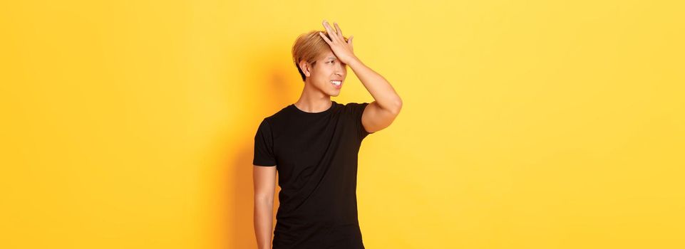 Upset and troubled asian guy snap forehead forgetful, standing over yellow background.