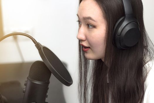 Young woman with microphone and headphones recording podcast at studio, professional record audio, technology and media concept, closeup