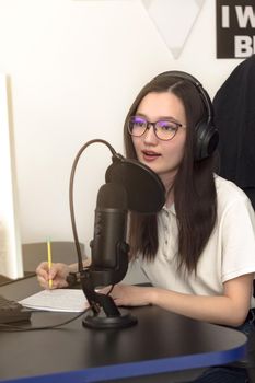 Young woman with glasses, microphone and headphones recording podcast at studio, professional record audio, technology and media concept, vertical image