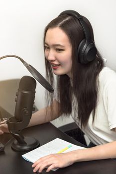 Young smiling woman with microphone and headphones recording podcast at studio, professional record audio, technology and media concept, vertical image