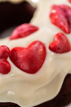 Freshly baked red velvet bundt cake with chocolate lips and hearts over cream cheese glaze for Valentine's Day.