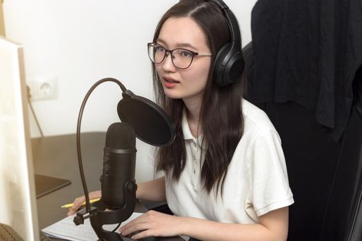 Young woman with glasses, microphone and headphones recording podcast at studio, professional record audio, technology and media concept