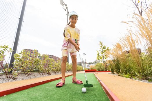 Cute preschool girl playing mini golf with family. Happy child having fun with outdoor activity. Summer sport for children and adults, outdoors. Family vacations or resort