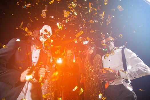 People dance at Halloween party with champagne glasses. Friends in the costumes in nightclub