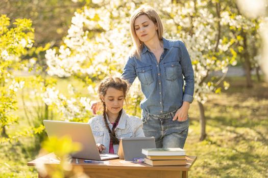 Beautiful mom with little daughter resting with a laptop in the park on a sunny day. Study, Learning, harmony, happiness, paradise - concept.