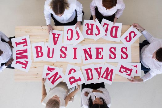 Businesspeople group in formal clothes merge letters on paper into word BUSINESS, cooperation unity startup concept