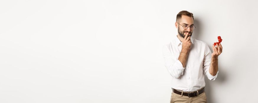 Happy man looking thoughtful at wedding ring in box, thinking about marriage proposal.