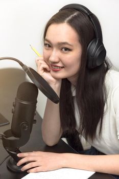 Young smiling woman with microphone and headphones recording podcast at studio, professional record audio, technology and media concept, vertical image