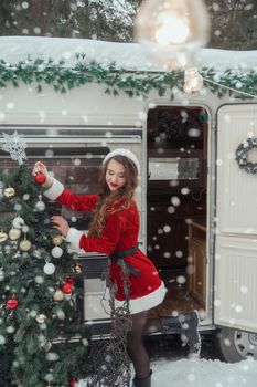 Young woman in santa costume decorates the Christmas tree at winter campsite getting ready for the new year. New year celebration concept