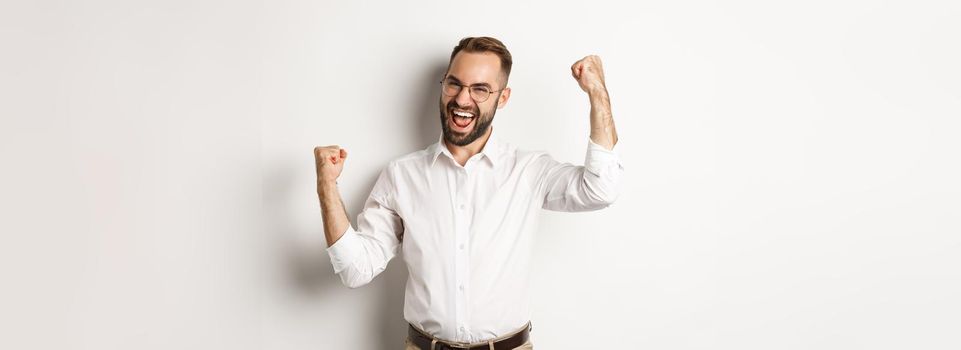 Successful businessman rejoicing, raising hands up and celebrating victory, winning something, standing over white background.