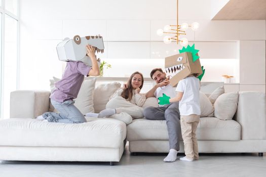 Happy family of parents and two children playing dinosaurs at home, children wearing handmade costume mask of cardboard