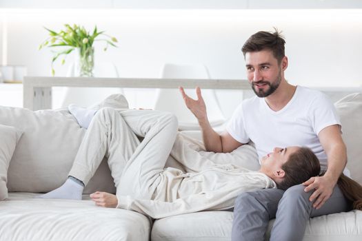 Woman lay head on boyfriend lap looking in each other eyes smile. Romantic husband and wife talking relaxing at home living room. Young affectionate married couple spend leisure time together