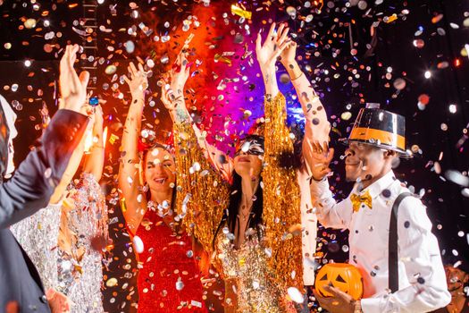 People dance at Halloween party with champagne glasses. Friends in the costumes in nightclub