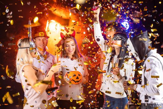 People dance at Halloween party with champagne glasses. Friends in the costumes in nightclub