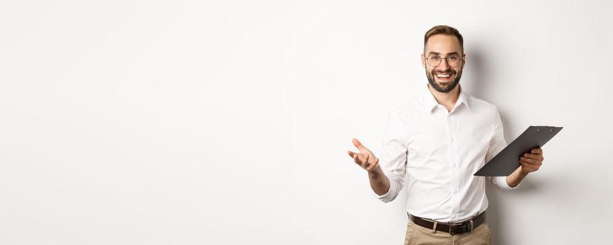 Handsome boss looking satisfied, holding clipboard and praising you, standing over white background.