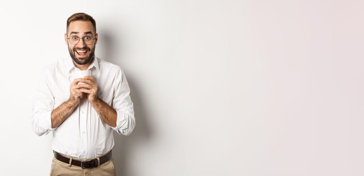 Man drinking coffee and looking excited, enjoying drink, standing over white background.