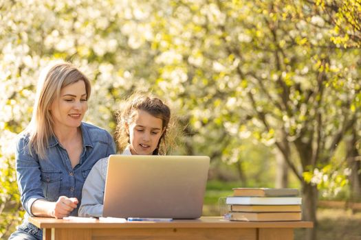 Woman and little girl laying on the spring flower field outdoors - having fun using a laptop