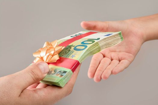 Money as a gift, prize or bonus. A man gives a bundle of money to a child. Banknotes of 100 euros are tied with a red ribbon with a bow