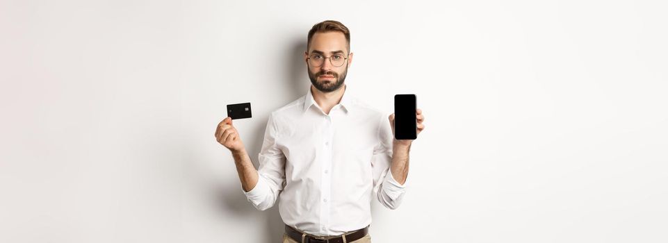 Serious business man showing mobile screen and credit card. Concept of online shopping.