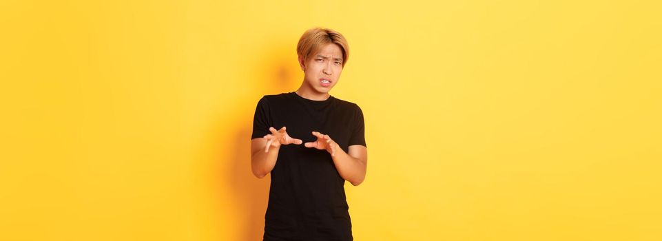 Portrait of disgusted picky asian guy, refusing and grimacing, standing yellow background.