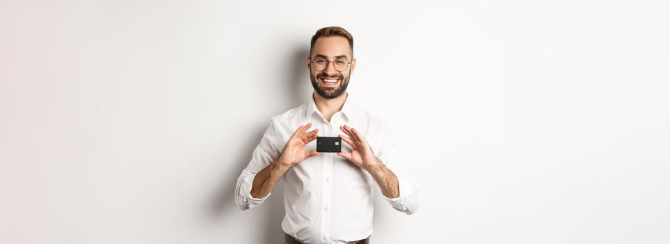 Handsome businessman holding a card, smiling satisfied, standing over white background.