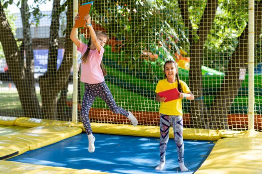 Two little girls in the summer jump on a trampoline, smiling and laughing. Children play. Relax in the fresh air. Friends jump on a trampoline. Happy child.