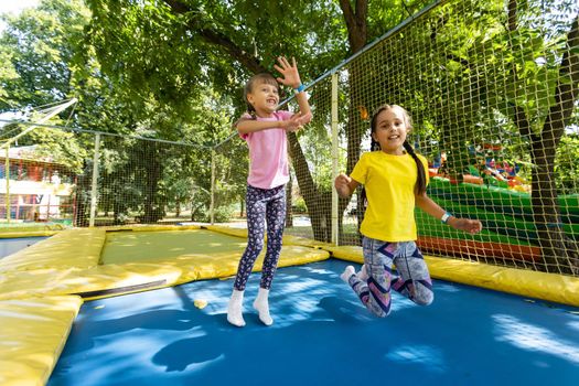 Two little girls in the summer jump on a trampoline, smiling and laughing. Children play. Relax in the fresh air. Friends jump on a trampoline. Happy child.