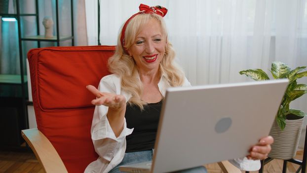 Overjoyed senior old grandmother on home chair with laptop scream in delight raise hands in triumph winner celebrate success win money in lottery. Excited elderly retired woman get online good news