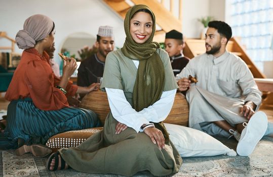 A happy Muslim woman sitting, with family and celebration of culture during Ramadan. A modern Islamic lady with a smile, beauty and in a hijab to celebrate holiday and eat together and home for Eid.