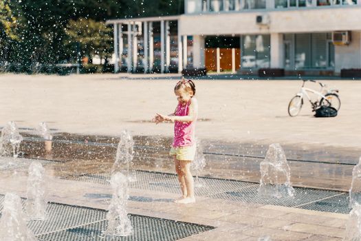 little girl playing with small fountains on the urban plaza