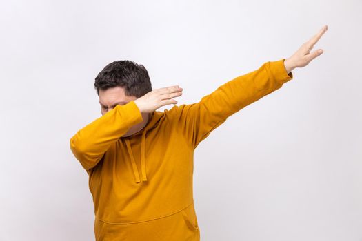 Portrait of dark haired anonymous man standing in dab dance pose, internet meme, celebrating success, wearing urban style hoodie. Indoor studio shot isolated on white background.