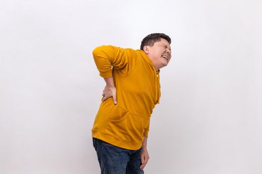 Spine problems. Middle aged man holding his back, having sudden lower back pain, pinched nerve or kidney inflammation, wearing urban style hoodie. Indoor studio shot isolated on white background.