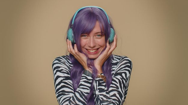 Happy pretty relaxed woman with purple coiffure hairstyle listening music via headphones and dancing disco fooling around having fun expressive gesticulating hands. Adult stylish female girl indoors