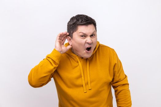 I can not hear you. Portrait of attentive handsome man standing with hand on ear and want to hear something, wearing urban style hoodie. Indoor studio shot isolated on white background.