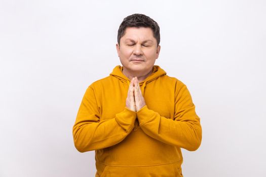 Yoga time. Portrait of middle aged handsome calm man standing in yoga pose and try to relaxing, keeps palms together, wearing urban style hoodie. Indoor studio shot isolated on white background.