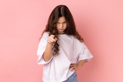 Portrait of angry little girl wearing white T-shirt noticing and pointing finger to camera, accusing with serious bossy face, making choice. Indoor studio shot isolated on pink background.