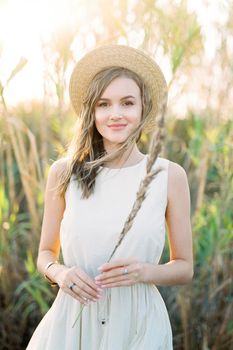 Girl in a straw hat stands with a dry cane in her hand. High quality photo