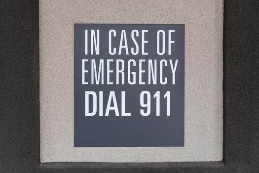 Gray sign on the wall depicting the emergency number, sign with inscription: in case of emergency dial 911