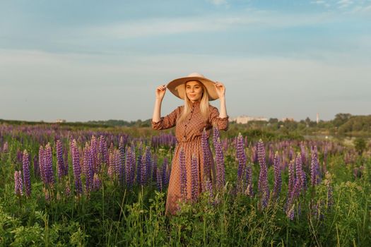 A beautiful woman in a straw hat walks in a field with purple flowers. A walk in nature in the lupin field.