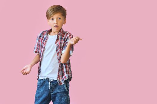 Young happy boy dressed in jeans, a white T-shirt and a plaid shirt with raised hands to the side isolated on pink background with copy space. Blank white t-shirt for your design