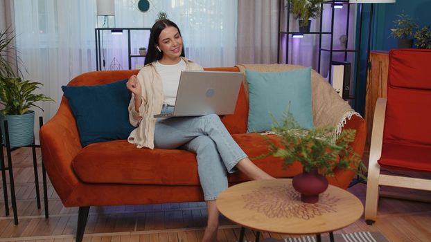 Portrait of caucasian girl sitting on couch, looking at camera, making video webcam conference call with friends or family, enjoying pleasant conversation. Young woman laughing, waving hello at home